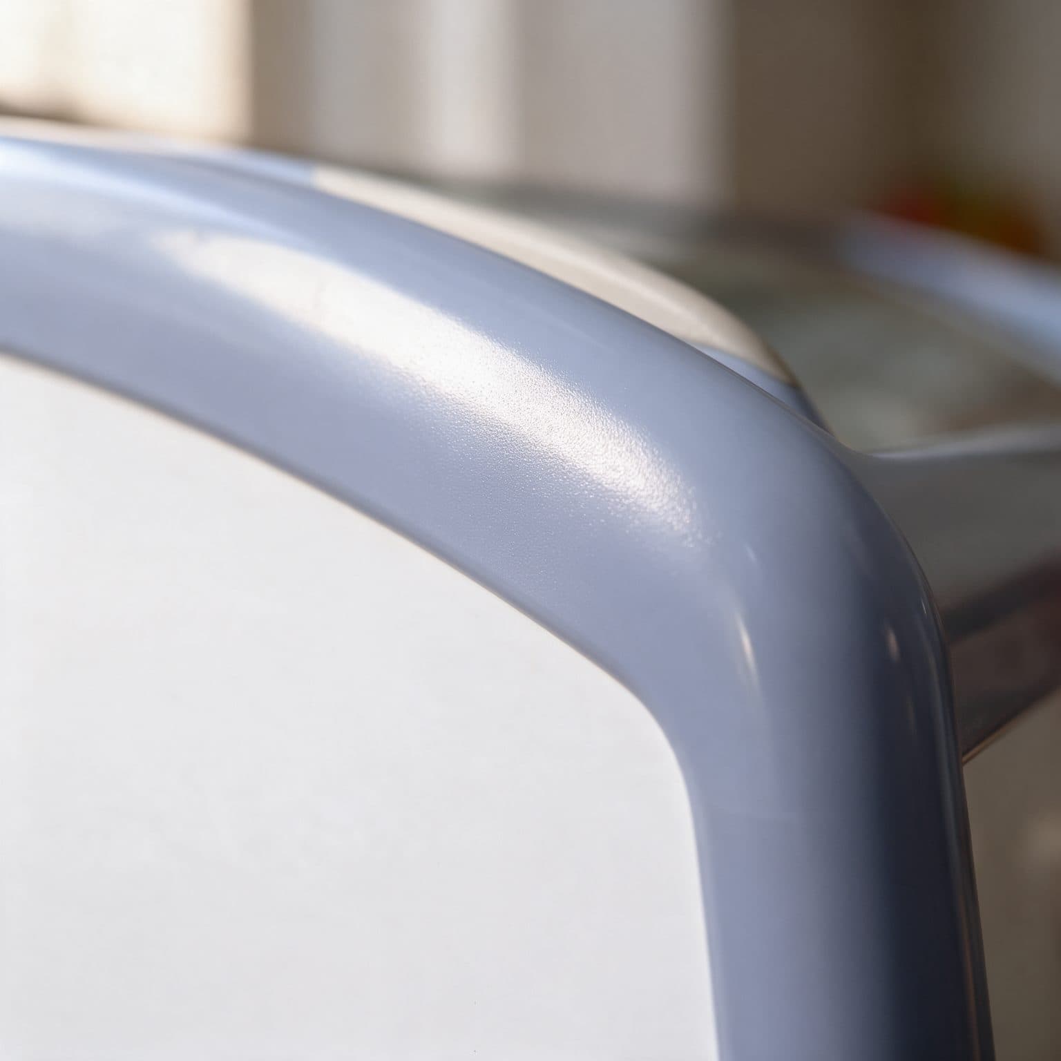 A close-up corner of a chest freezer's light blue-grey ABS frame, curving from the glass lid rail down to the white cabinet body, with soft daylight and a blurred glass lid and wire baskets behind.