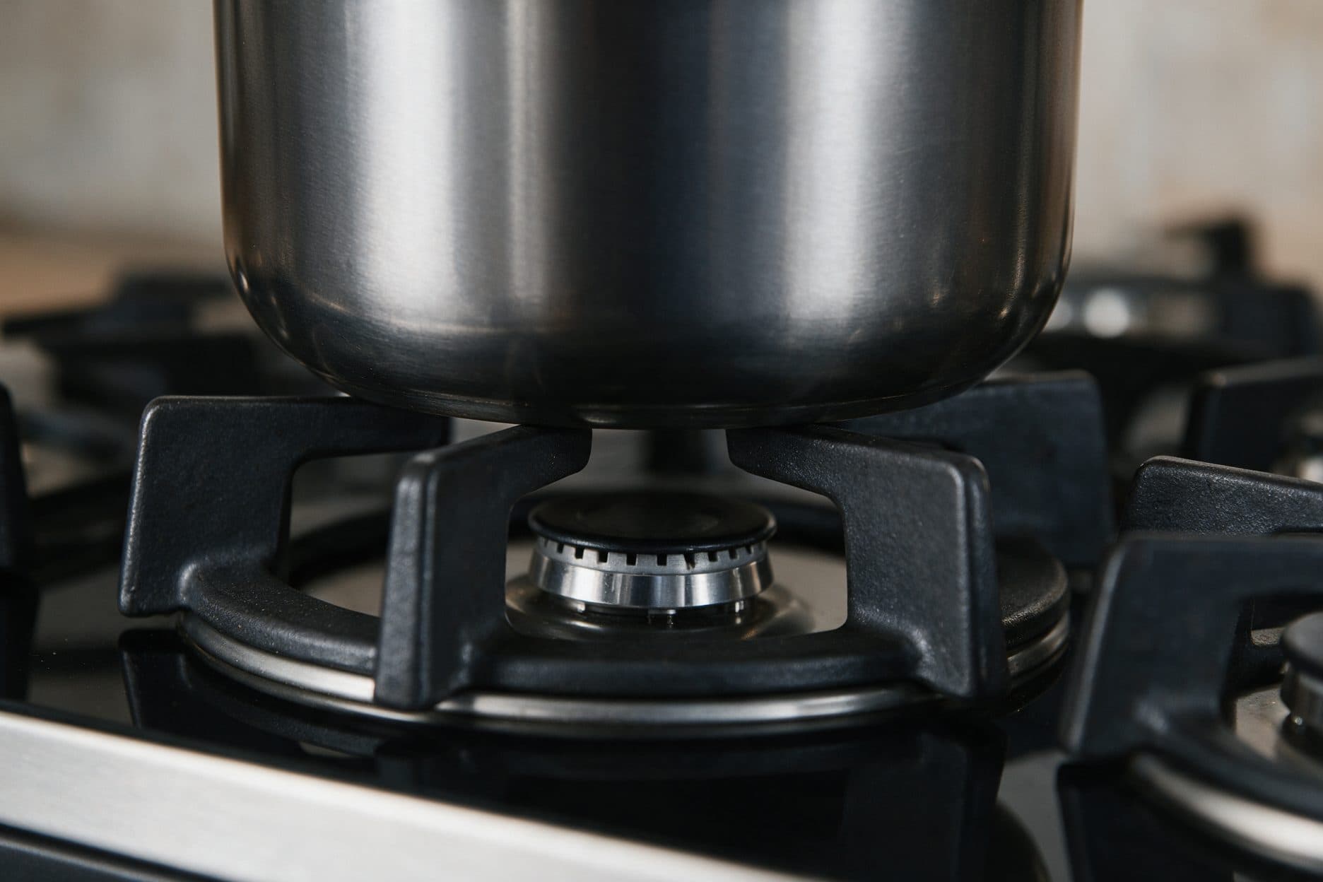 A heavy dark metal pot rests directly on the arms of a matte black cast-iron pan support over a gas burner, with the burner cap visible underneath between the support arms.