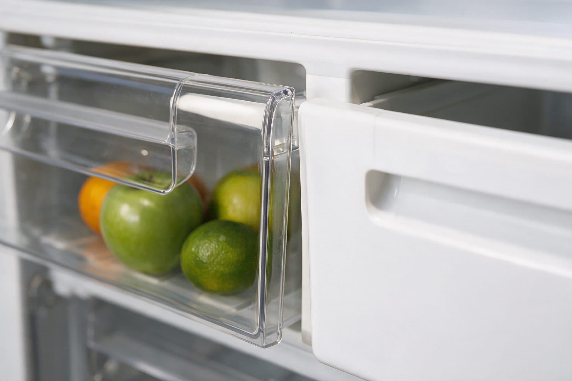 A clear crystal drawer and a white opaque drawer sit side by side in the fridge, both holding fresh citrus and apples.