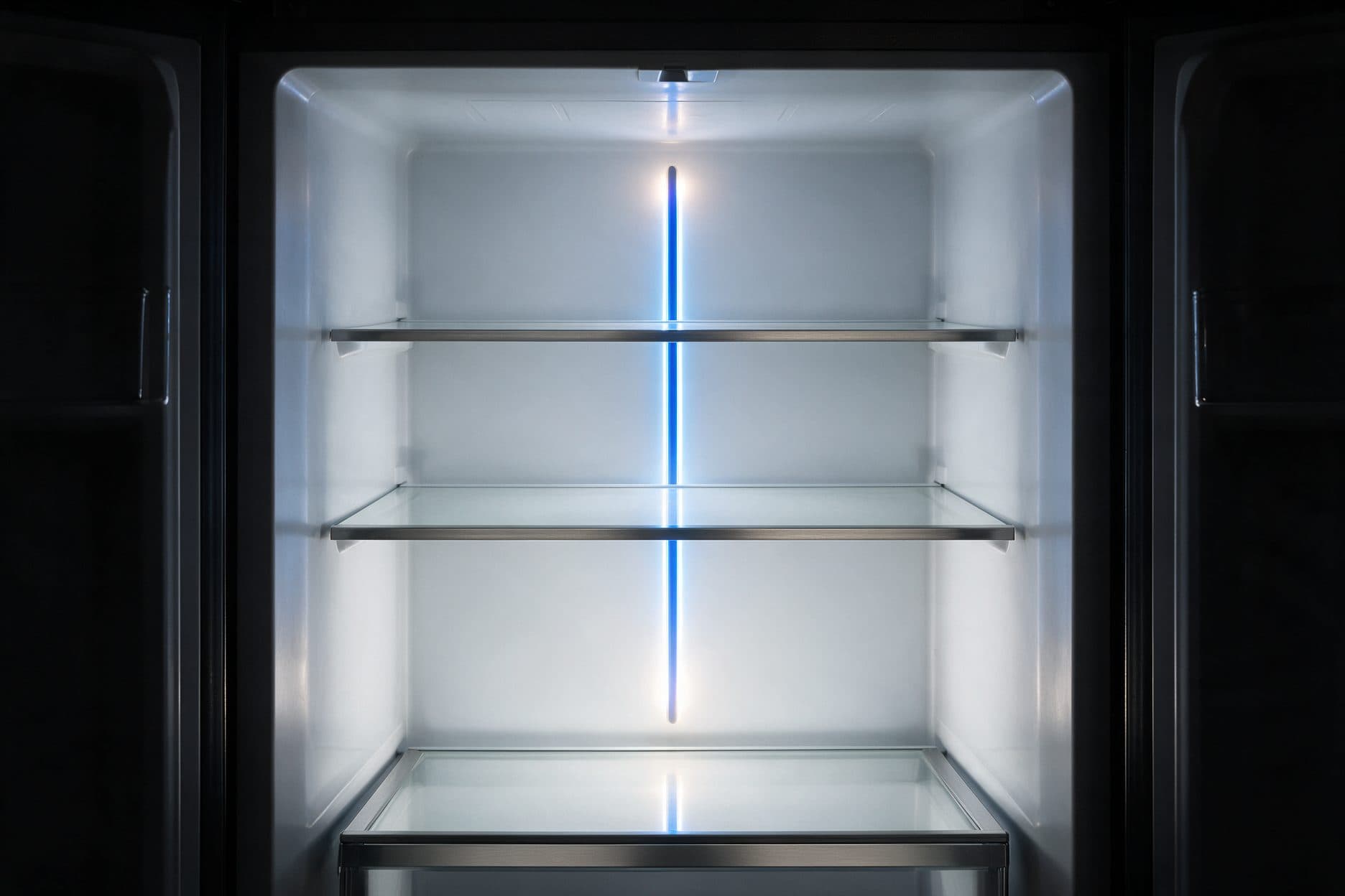A nearly black fridge cavity, its two glass-and-chrome-trim shelves and the base drawer, is lit top to bottom by one slim blue-white LED strip running down the center of the back wall.